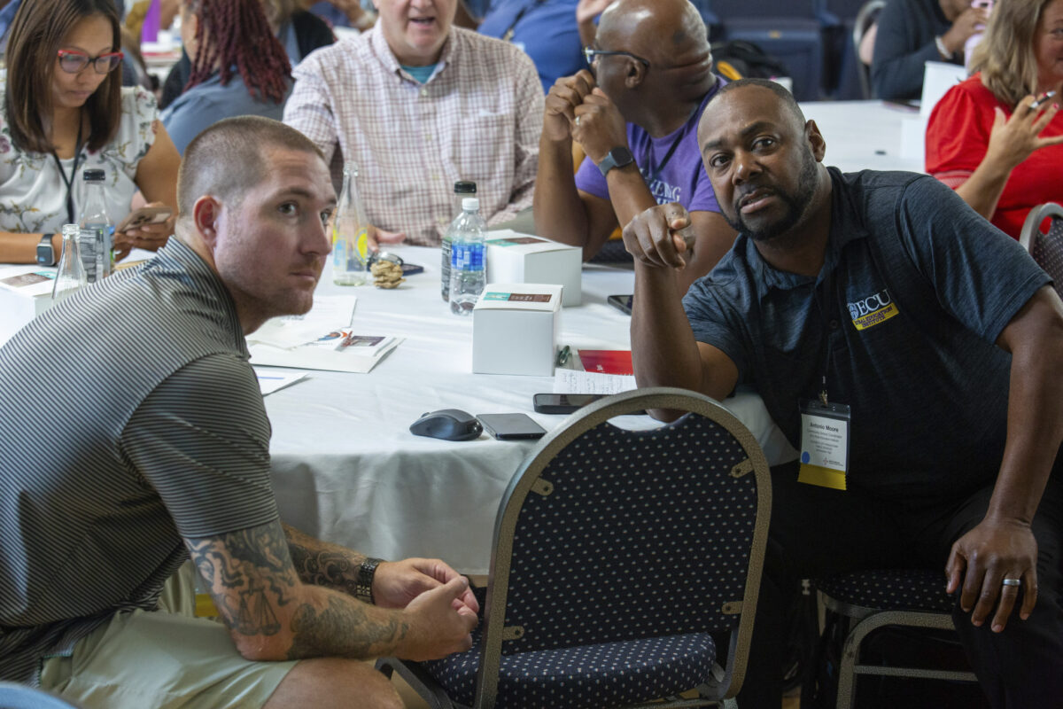 Two men (Wilson and Antonio) sitting at table with others at NCCSC at the leadership summit